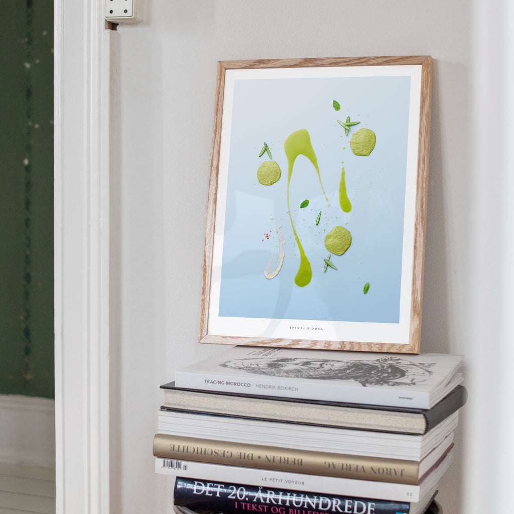 Spinach Dosa art print on a stack of books against a white wall.