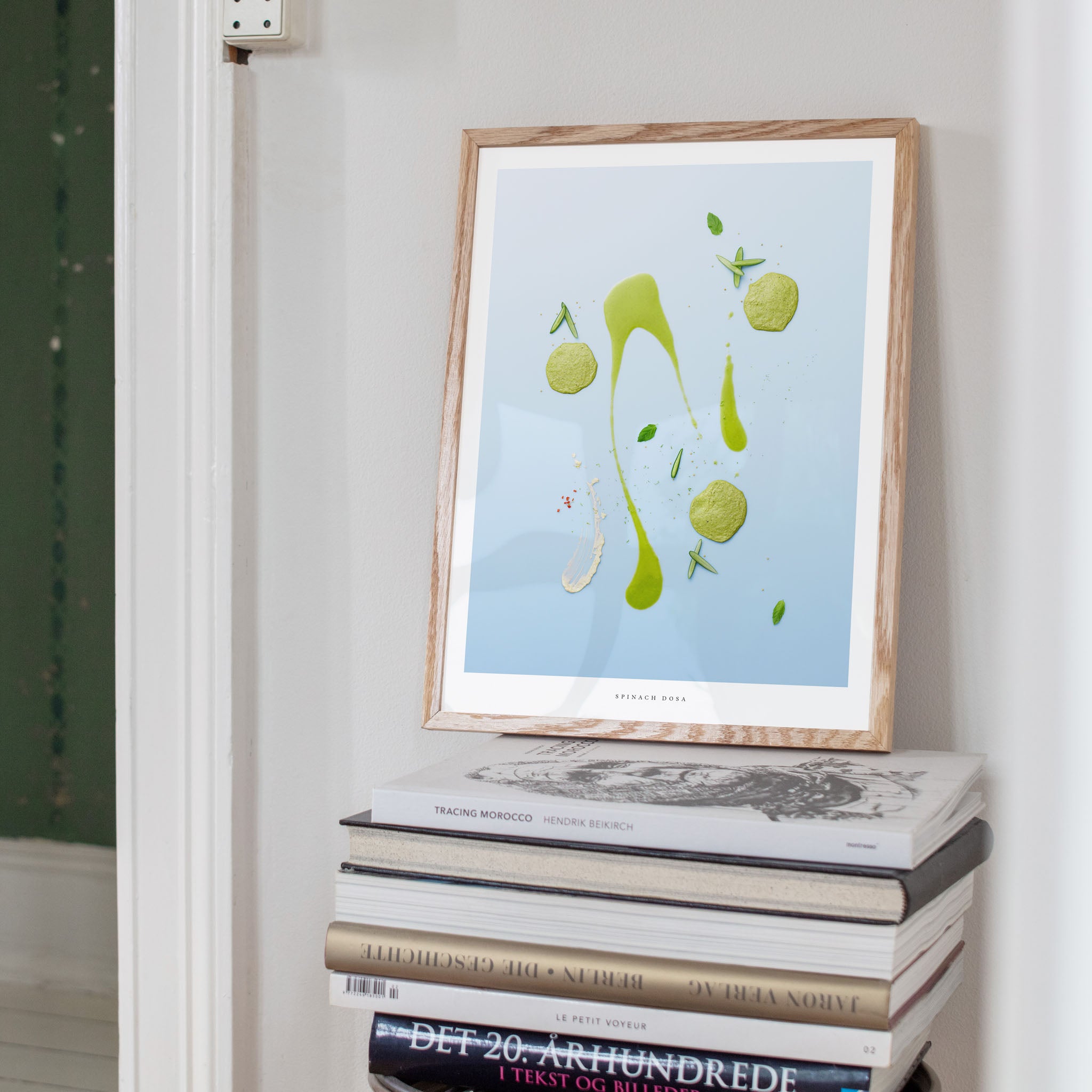 Spinach Dosa art print on a stack of books against a white wall.