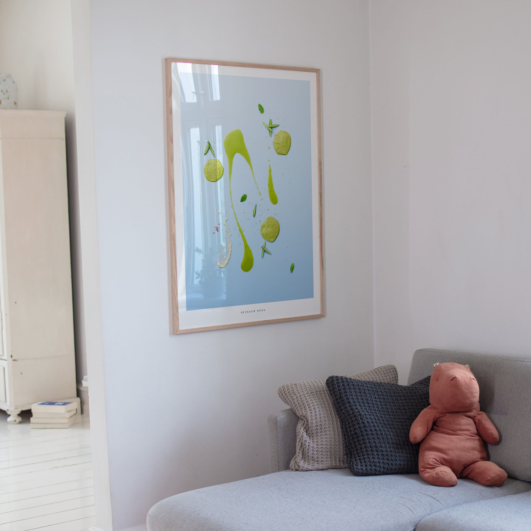 Framed artwork on a wall above a sofa with cushions and a teddy bear.