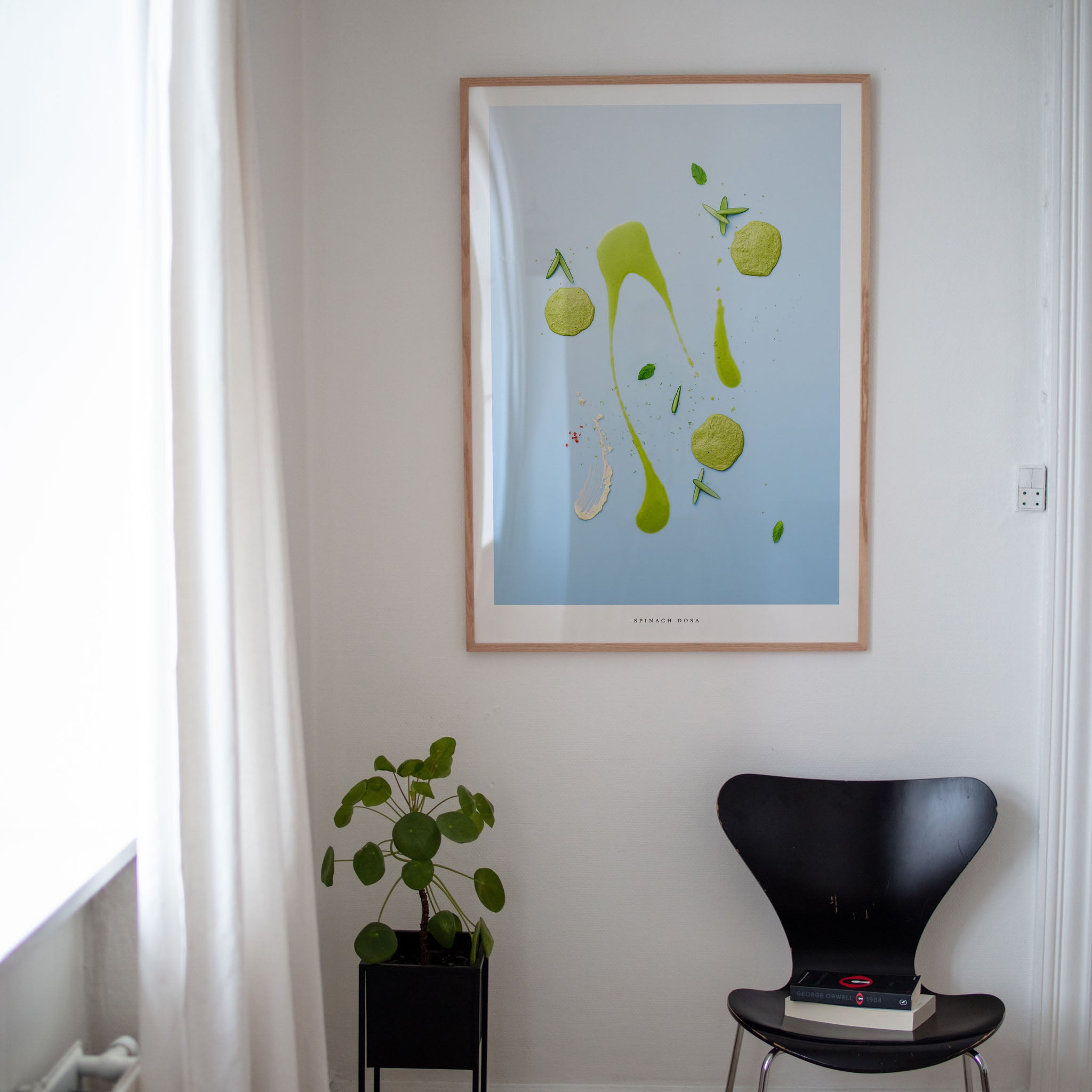 Spinach Dosa poster on white wall with plant and black chair