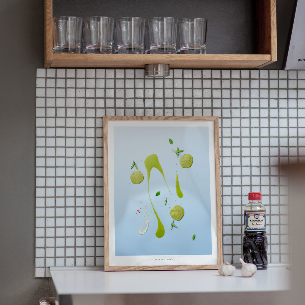 Framed artwork on a kitchen counter with tiled wall and shelf in the background