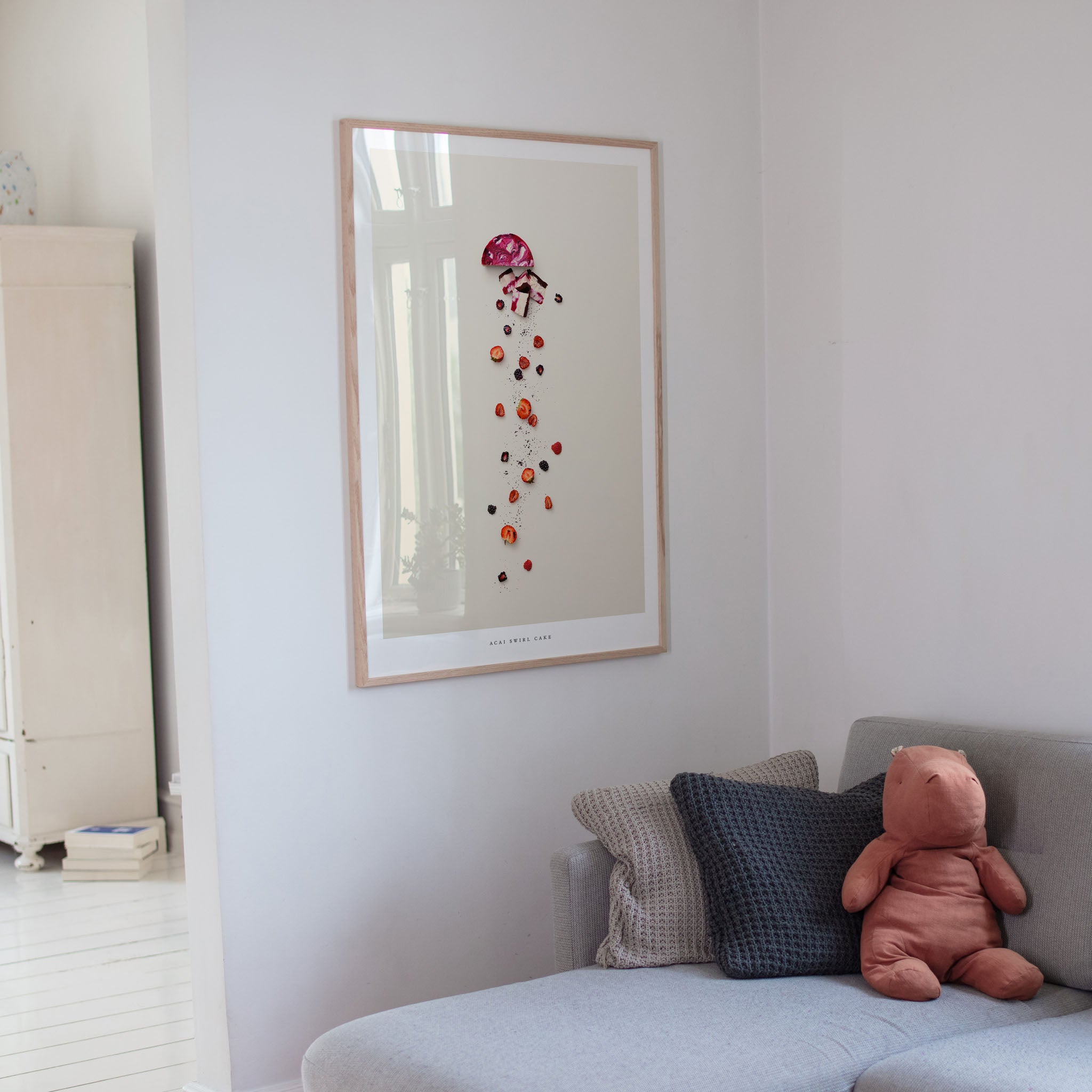 Framed artwork on a wall above a sofa with cushions and a teddy bear.