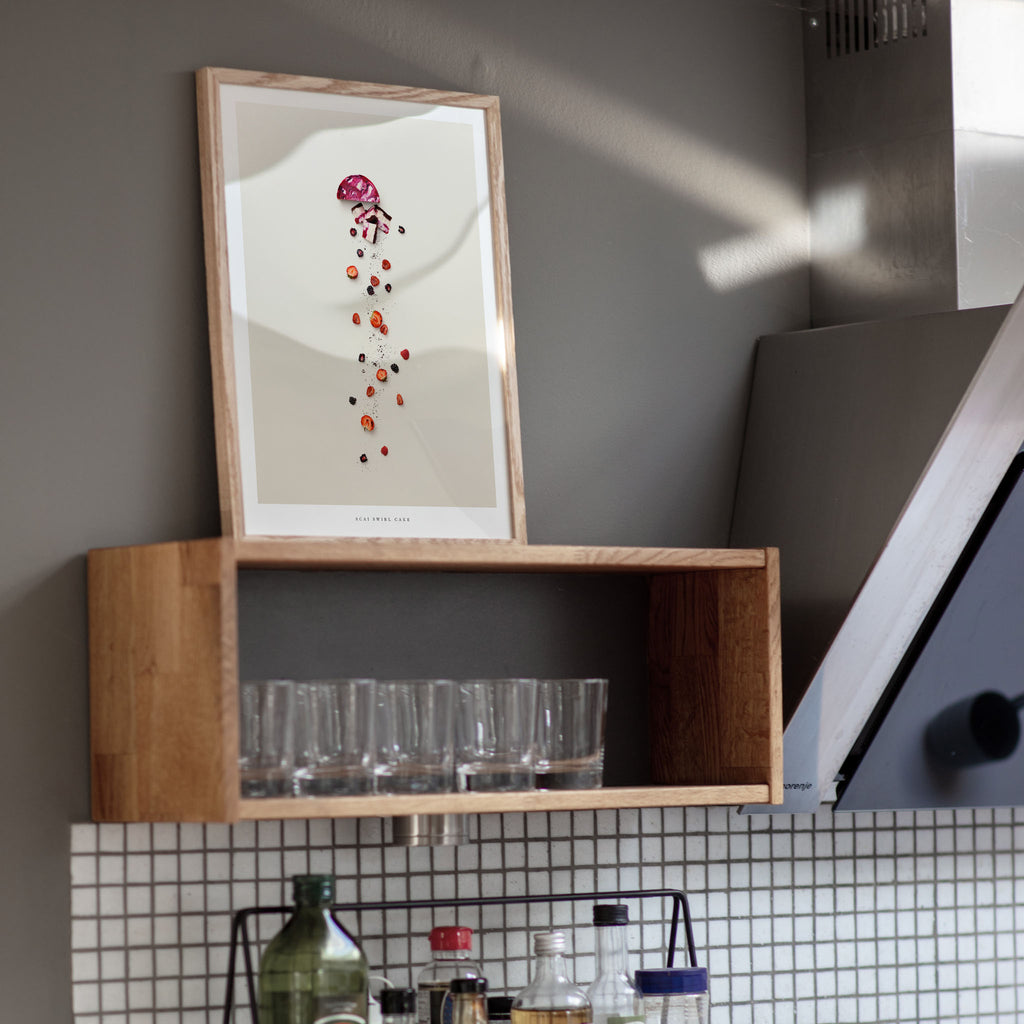Wooden kitchen shelf with glasses above a tiled wall, Acai Swirl Cake poster on the wall.