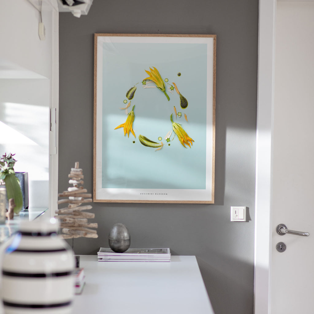 Zucchini Blossom art print on a gray wall with decorative items on a table.